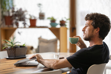 Happy young man in his moment of relaxation turns off the laptop holding a cup of hot milk coffee with his hands, latte art, in his favorite cafe, he enjoys the aroma of coffee and it gives him energy