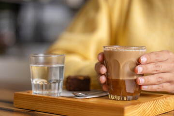 Young woman enjoys her breakfast or lunch, recovering energy with a delicious caramel coffee and eats a chocolate cupcake, close-up in a specialized pastry cafe on a wooden table
