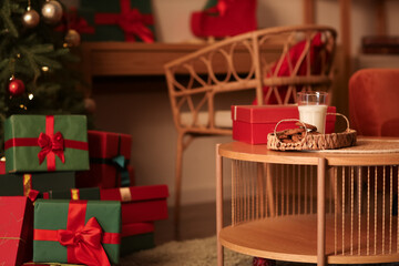 Table with cookies, glass of milk and Christmas presents in room at night