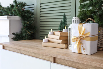 Gift box, books and glowing electrical candles on chest of drawers in living room