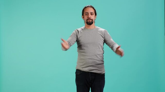 Man wearing casual clothing covering eyes, ears and mouth, imitating three wise monkeys, doing dont see, dont hear and dont speak hand gesturing concept, blue studio backdrop, camera A