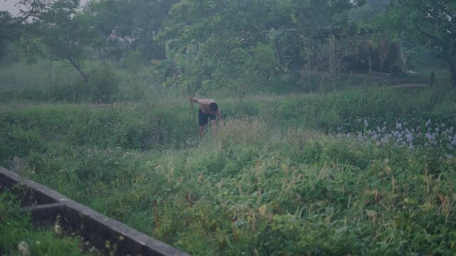 young asian man works with hoe in a crop area in vietnam at dusk