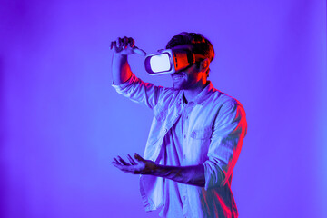 Side view of happy man holding and moving gesture while using VR goggle. Happy person using headset and goggle while enter virtual world or metaverse with neon light background. Technology. Deviation.