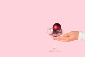 Female hand with glass of beautiful Christmas balls on pink background, closeup