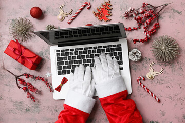 Santa hands with modern laptop, Christmas decorations and gift on color grunge background