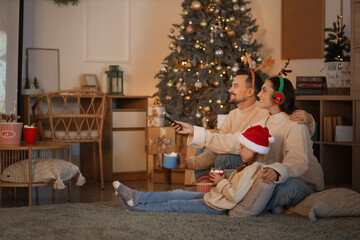 Little girl with cocoa and her parents watching Christmas movie on projector screen at home