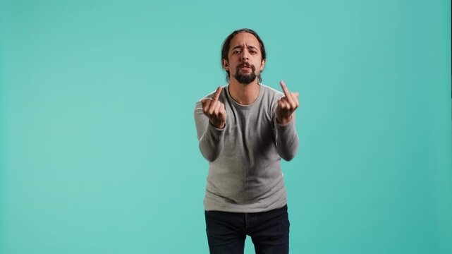 Irked man fighting with friend, doing middle finger sign gesturing, isolated over studio background. Outraged person arguing during conversation, doing obscene hand gestures, camera A