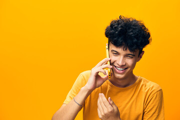 Young man talking on the phone with a bright smile against a vibrant yellow background, showcasing...