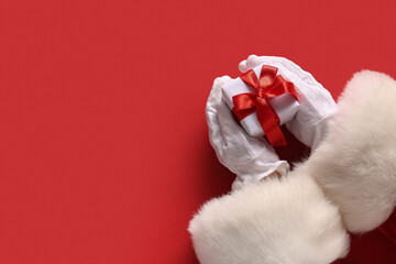 Santa hands with Christmas gift box on red background, closeup