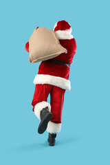 Santa Claus with Christmas bag running on blue background, back view