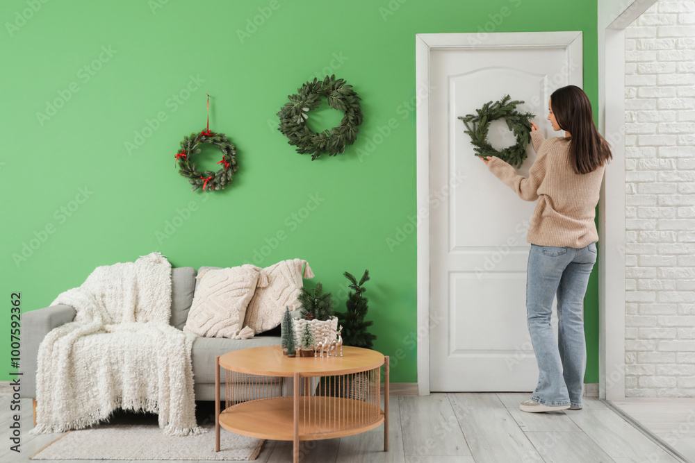 Sticker Woman hanging Christmas wreath on door at home, back view