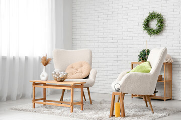 Armchairs, coffee table with pampas grass in vase and Christmas decorations near white brick wall