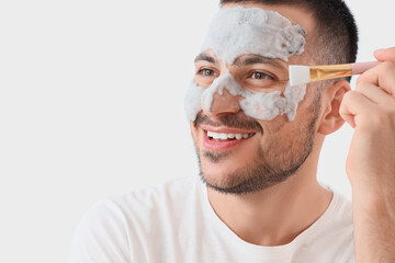 Handsome young happy man applying cosmetic bubble mask on face against grey background