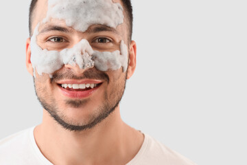 Handsome young happy man with cosmetic bubble mask on face against grey background
