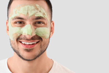 Handsome young happy man with cosmetic bubble mask on face against grey background