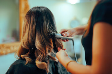 Hairstylist Using Hair Straightener for Curling Hair in a Salon. Lady having her hair styled after...