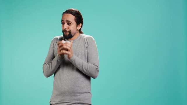 Man closes eyes while tasting and enjoying delicious coffee, isolated over blue studio backdrop. Person drinks caffeinated beverage to gain energy and be able to do doing productivity tasks, camera B