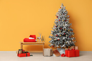 Decorated Christmas tree with gift boxes, bench with Santa hat, sack, reindeer and decor near yellow wall