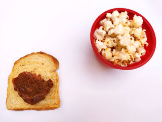 Isolated toast with jam and popcorn on the red bowl on the white background
