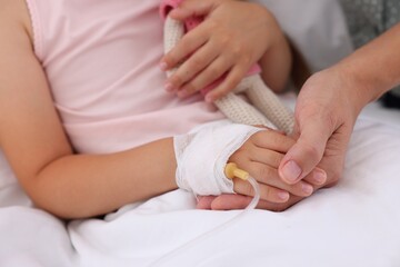 Mother and her little daughter with IV drip on bed in hospital, closeup