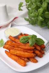 Sweet potato fries, basil and sauce on light grey table, closeup