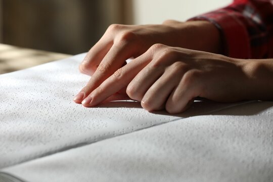Blind woman reading book written in Braille at table, closeup