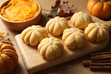 Raw pumpkin shaped buns and ingredients on brown table