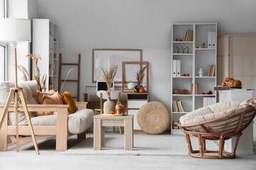 Interior of light living room with autumn decor, sofa and workplace