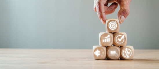 Hand arranging wooden blocks with business icons symbolizing an action plan concept on a wooden...