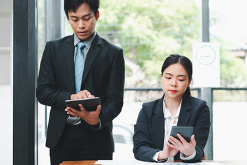 Two business professionals in formal attire working together using digital devices in a modern office setting.
