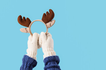 Woman in warm gloves with reindeer horns on blue background © Pixel-Shot
