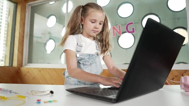 Cute girl using laptop programing software while looking and laughing at camera. Pretty child smiling while giving thump up with funny innocent mood in Stem class. Smart student portrait.Erudition.