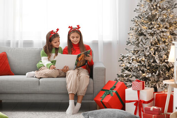 Cute happy little girls in reindeer horns  with book reading Christmas story on sofa at home