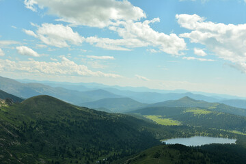 View from the top of the mountain flat valley and a fragment of a picturesque lake in the lowland under the summer cloudy sky.
