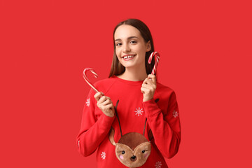 Young woman in Christmas sweater with candy canes on red background