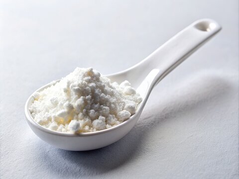 Close-up of a white powder of magnesium stearate, a common pharmaceutical lubricant, in a small scoop or spoon on a clean white laboratory background.