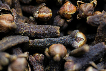 A close-up texture of freshly dried clove spices scattered on the ground. Cloves serve as a dried herb for food flavoring and natural medicine. Dry Organic Clove Spice.