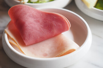 A variety of assorted slices of delicious cold cut ham arranged elegantly in a white bowl