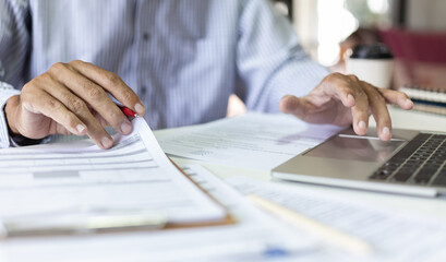 Asian businessman reviewing document report at office working with laptop, professional lawyer reading and checking financial documents or insurance contract before sign, Close-up shot