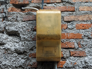 An old, weathered electrical box mounted on a rough, textured brick wall. The contrast between the worn yellow box and the rustic wall creates an industrial and urban aesthetic.