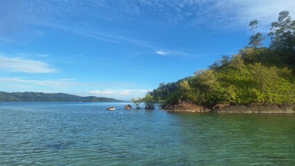 Fototapeta premium beautiful view of clear sea with a background island and hills. Blue sky and slightly cloudy. The picture was taken from the middle of the sea. West Sumatra, Indonesia