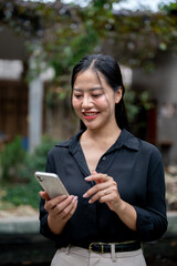 Fototapeta premium A charming Asian businesswoman is reading text messages on her smartphone in a garden space.