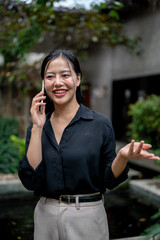 A charming Asian businesswoman is having a conversation on the phone while relaxing in a garden.