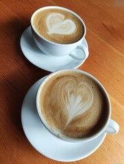 Two cups of coffee with hearts on the wooden surface