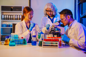 Fototapeta premium middle-aged man, an old woman, and a young woman collaborate in a lab at night, under blue and RGB lighting, researching food ingredients and conducting experiments with test tubes and microscopes.