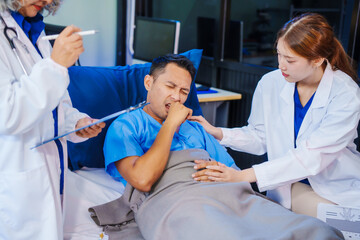 A middle-aged man lies bedridden on hospital bed, closely monitored by an old Asian woman doctor and young nurse. They assess his symptoms, including heart and lung conditions, offer advice.