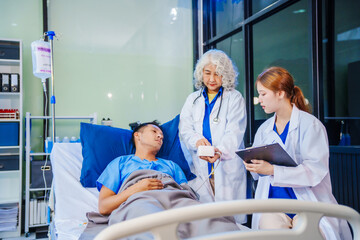 Fototapeta premium A middle-aged man lies bedridden on hospital bed, closely monitored by an old Asian woman doctor and young nurse. They assess his symptoms, including heart and lung conditions, offer advice.