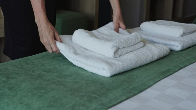 Female hands in a hotel room lay out fresh and clean towels for guests. Hotel service, maid prepares the room for travelers to check in. Hospitality
