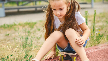 Modern little girl sitting on skateboard in the sport field. Active kids. Sports. Entertainment.