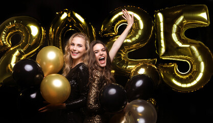 Happy gorgeous girls in stylish sexy party dresses holding gold 2025 balloons, having fun at New...